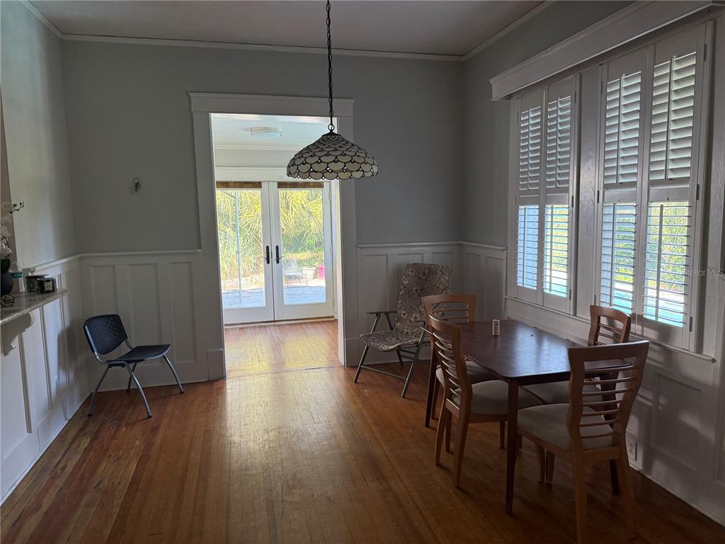 A dining room features hardwood floors, wainscoting, a pendant light, and a view of a patio — 404 NE 10TH AVENUE, GAINESVILLE, FL