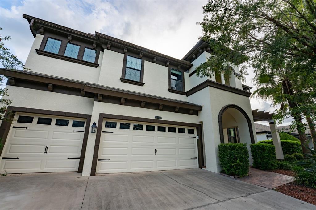 A two-story house exterior features a three-car garage, stucco walls, and a covered entryway — 8355 SWISS CHARD CIRCLE, LAND O LAKES, FL
