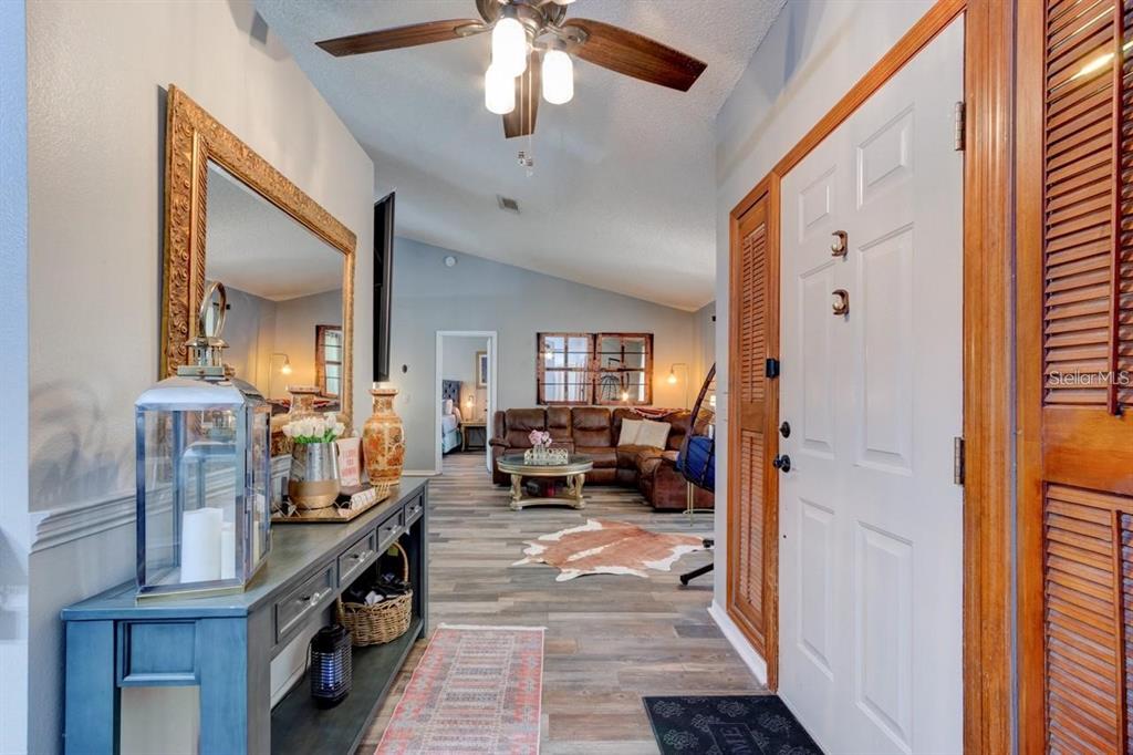 An entryway leads into a living room with wood-look flooring, a ceiling fan, and furniture — 3237 NEWMARK DRIVE, DELTONA, FL