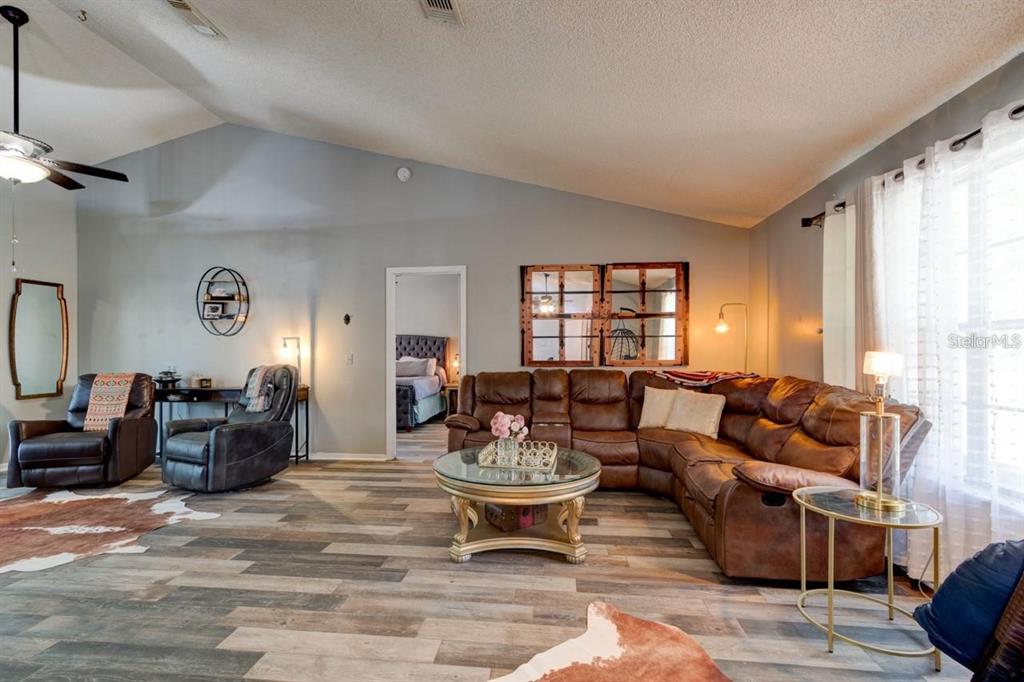 A living room features a brown leather sectional, two recliners, and wood-look flooring — 3237 NEWMARK DRIVE, DELTONA, FL