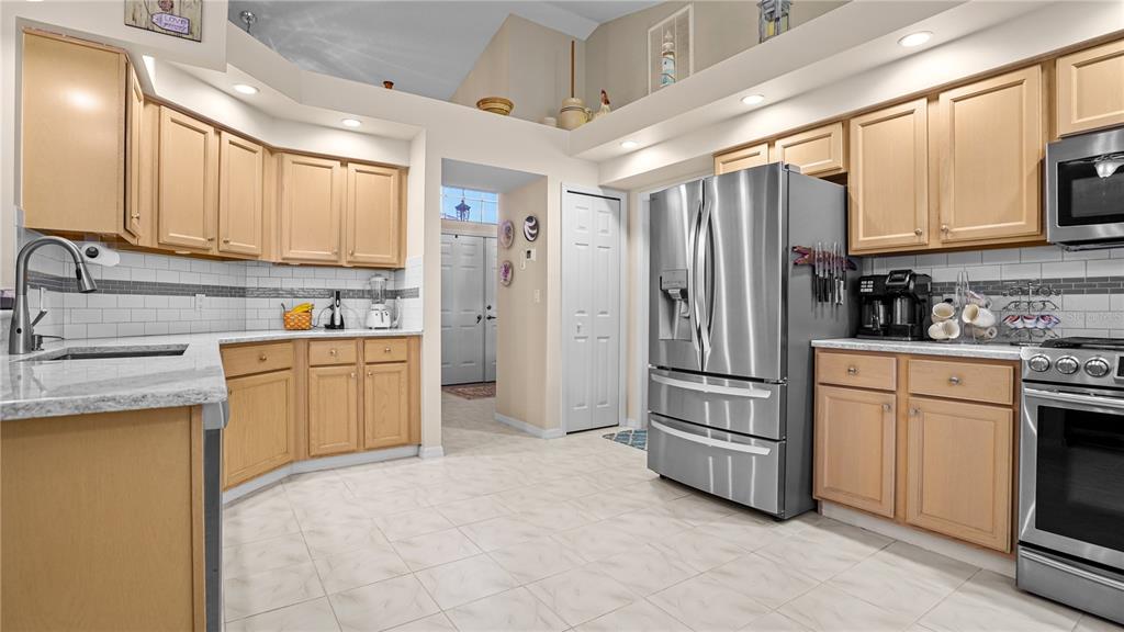 A kitchen features light wood cabinets, stainless steel appliances, granite countertops, and white tile flooring — 9221 HALBERG DRIVE, HUDSON, FL
