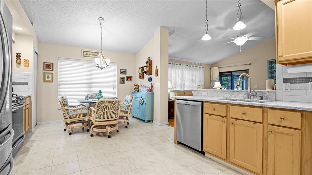 A kitchen with light wood cabinets, granite countertops, and an adjacent dining area with wicker chairs — 9221 HALBERG DRIVE, HUDSON, FL