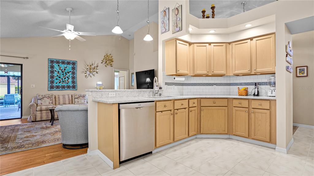 A kitchen with light wood cabinets and granite countertops overlooks a living area with tile — 9221 HALBERG DRIVE, HUDSON, FL
