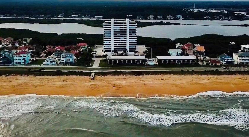 An aerial view shows a tall white condominium building situated between a beach and a waterway — 1601 N CENTRAL AVENUE UNIT 101, FLAGLER BEACH, FL