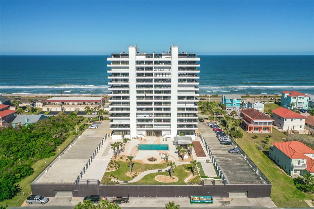 An aerial view shows a tall white beachfront condominium building with a pool and parking — 1601 N CENTRAL AVENUE UNIT 101, FLAGLER BEACH, FL