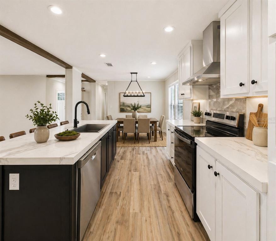 A modern kitchen with a black island, white cabinets, and wood-look flooring leads to a dining area — 202 MIMOSA DRIVE, HAWTHORNE, FL