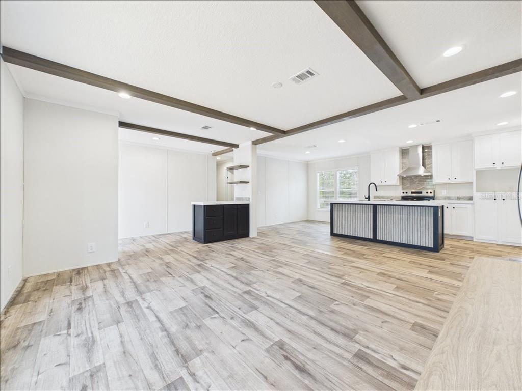 An open-concept kitchen and living area features wood-look flooring, white cabinets, and ceiling beams — 202 MIMOSA DRIVE, HAWTHORNE, FL