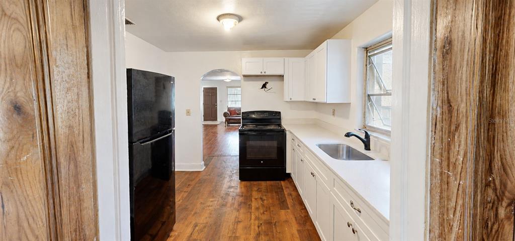 A small, sparsely furnished room with white walls, hardwood floors, and a closed white door — 415 MODEL STREET, DAYTONA BEACH, FL