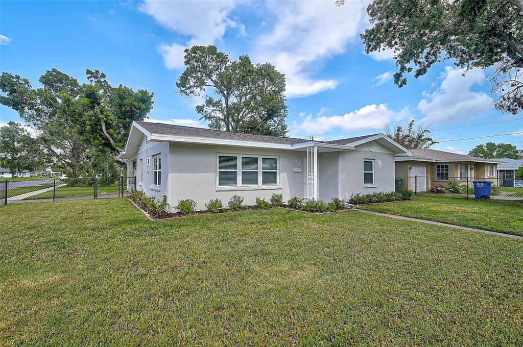 A single-story light gray house with a large front lawn and a black chain-link fence — 102 20TH STREET NE, BRADENTON, FL