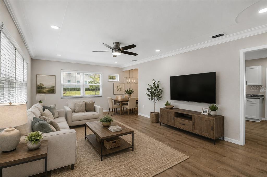 A living room with wood-look flooring, a ceiling fan, a television, and an adjacent dining area — 102 20TH STREET NE, BRADENTON, FL