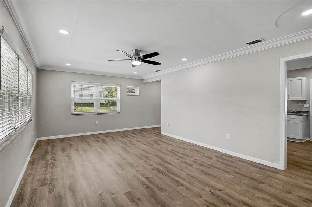 An empty living room features light wood-look flooring, gray walls, a ceiling fan, and windows — 102 20TH STREET NE, BRADENTON, FL