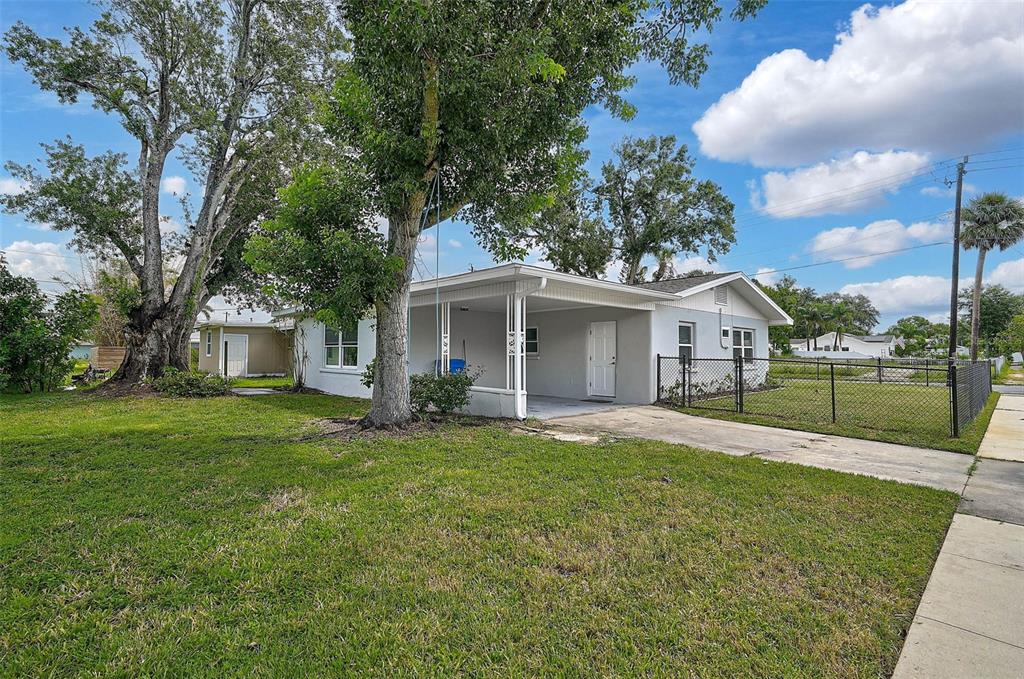 A single-story house with a carport, a large tree in the yard, and chain-link fencing — 102 20TH STREET NE, BRADENTON, FL