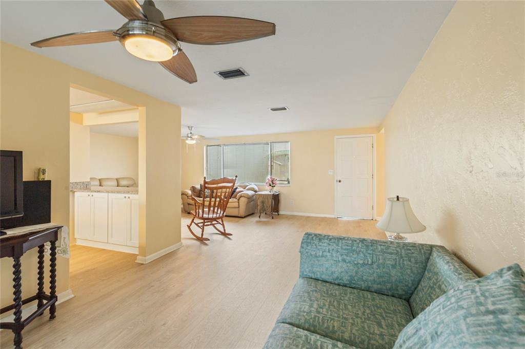 A living room features light wood-look flooring, pale yellow walls, and a ceiling fan — 3228 ROCK VALLEY DRIVE, HOLIDAY, FL