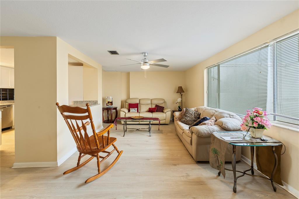 A living room features light-colored wood flooring, two beige sofas, a wooden rocking chair, and blinds — 3228 ROCK VALLEY DRIVE, HOLIDAY, FL