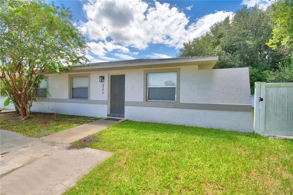 A single-story house with a white stucco exterior, gray trim, and a small front lawn — 914 GRAPE AVENUE, ST CLOUD, FL