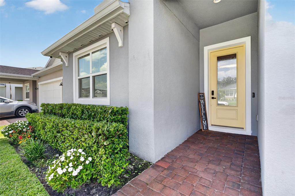 A gray house exterior features a yellow front door, brick walkway, and landscaped bushes — 3607 ARBORDALE LOOP, SANFORD, FL