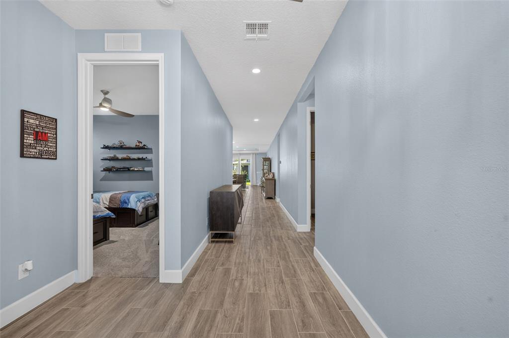 A hallway with light blue walls and wood-look tile flooring leads toward a living area — 3607 ARBORDALE LOOP, SANFORD, FL