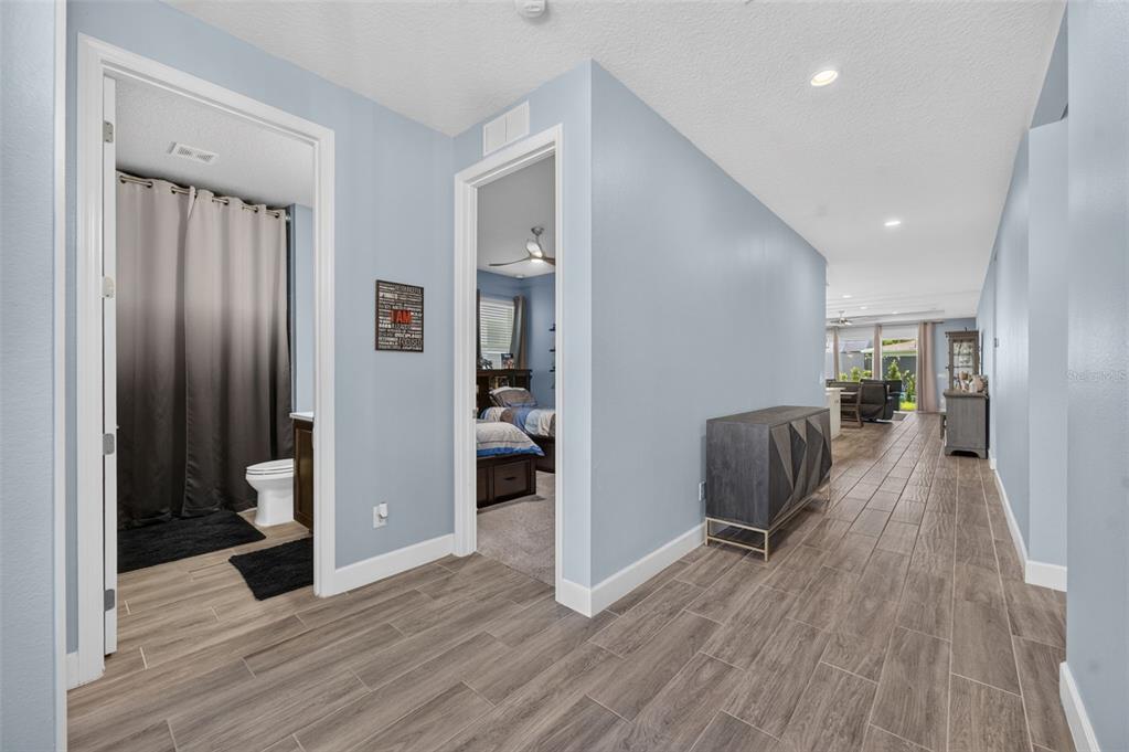 A hallway with wood-look tile flooring leads to a bedroom, bathroom, and open living area — 3607 ARBORDALE LOOP, SANFORD, FL