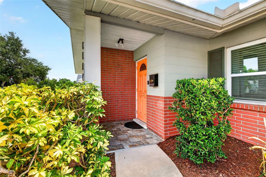 A front entryway features a bright orange door, red brick accents, and a tiled porch — 3409 18TH AVENUE DRIVE W, BRADENTON, FL