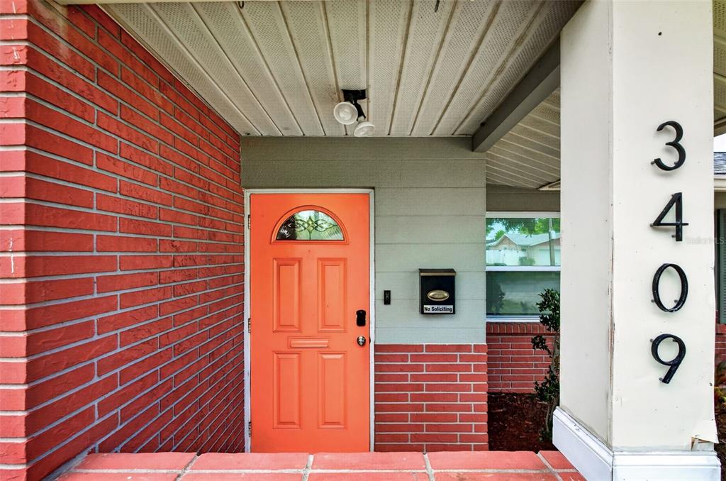 A bright orange front door is set into a brick and gray exterior entryway — 3409 18TH AVENUE DRIVE W, BRADENTON, FL