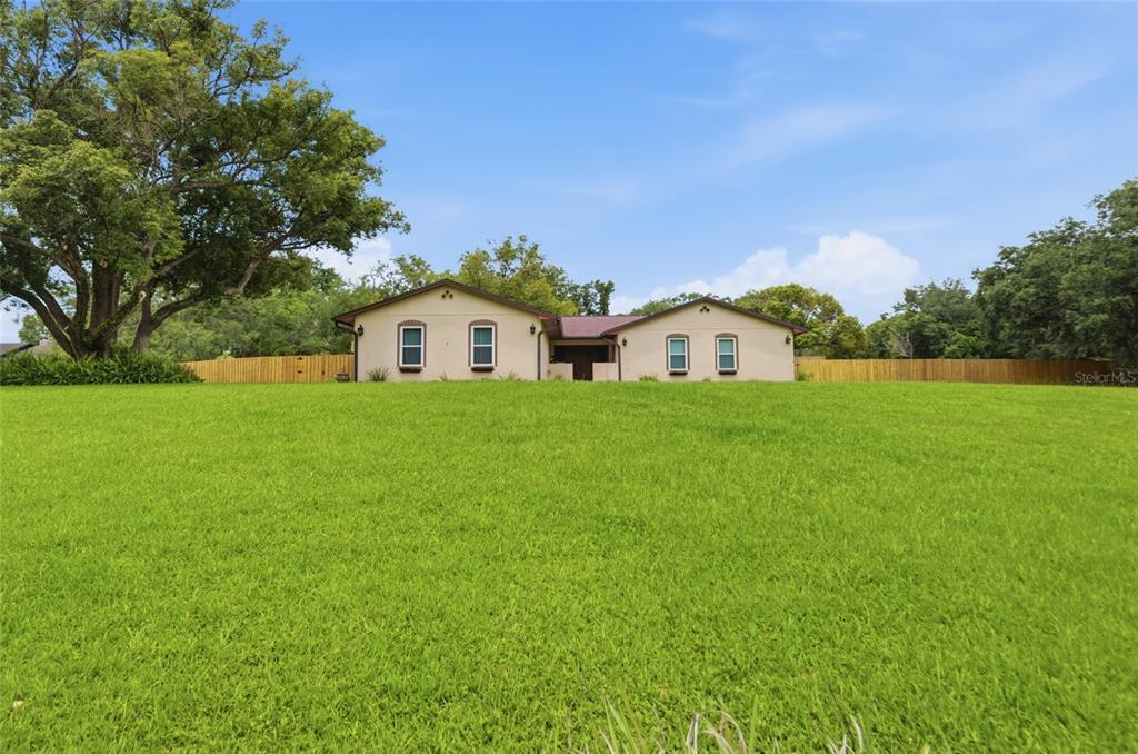 A single-story house with a light-colored exterior sits behind a large, open grassy lawn — 6538 NIGHTWIND CIRCLE, ORLANDO, FL