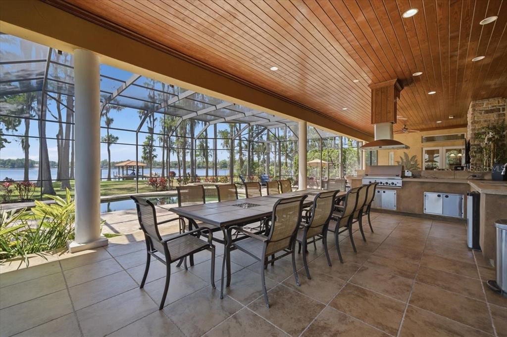 A covered outdoor patio features a dining table, an integrated kitchen, and a screened pool — 18258 WAYNE ROAD, ODESSA, FL