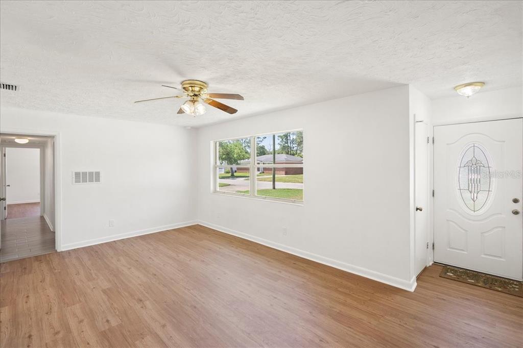 An empty living room with wood-look flooring, a ceiling fan, and a white front door — 2125 W LOU DRIVE, JACKSONVILLE, FL