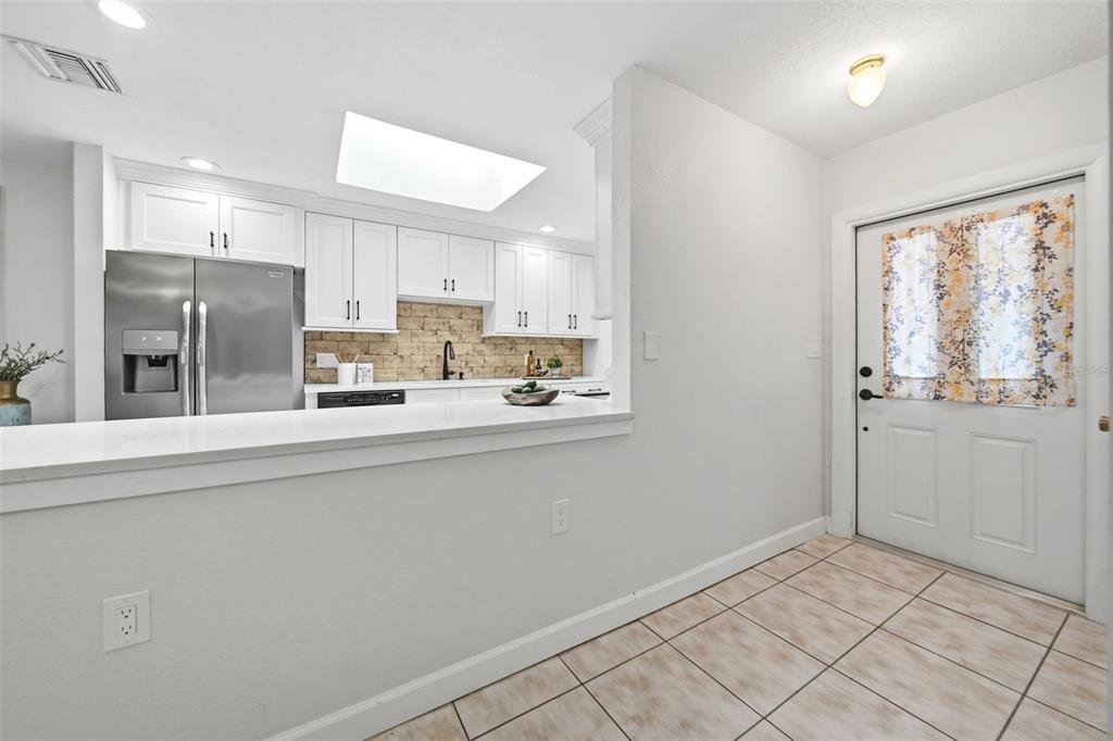 A kitchen with white cabinets and stainless steel appliances overlooks a tiled entryway with a door — 1540 E HORATIO AVENUE, MAITLAND, FL