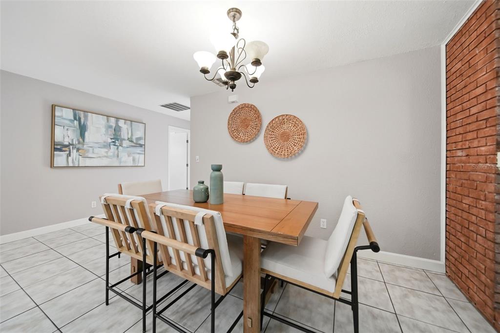 A dining room features a wooden table, chairs with white cushions, and a brick wall — 1540 E HORATIO AVENUE, MAITLAND, FL