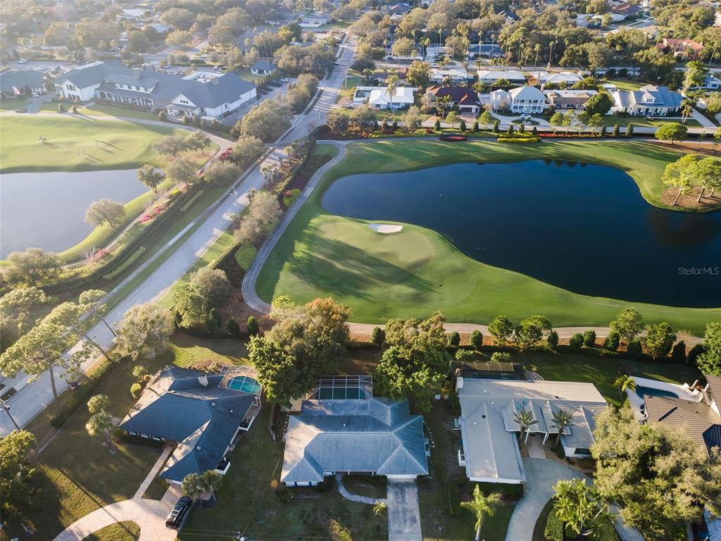 An aerial view shows houses with pools overlooking a golf course and a large pond — 4 HIBISCUS ROAD, BELLEAIR, FL