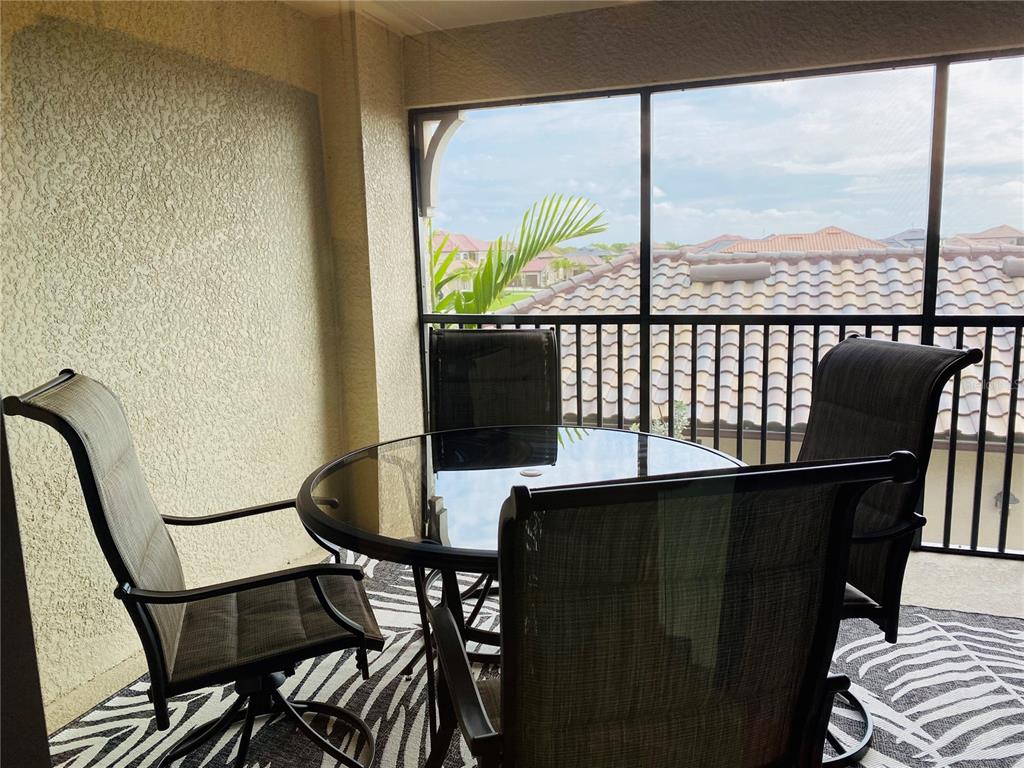 A screened-in balcony features a glass-top table, four chairs, and a patterned rug — 5664 PALMER CIRCLE UNIT 202, BRADENTON, FL