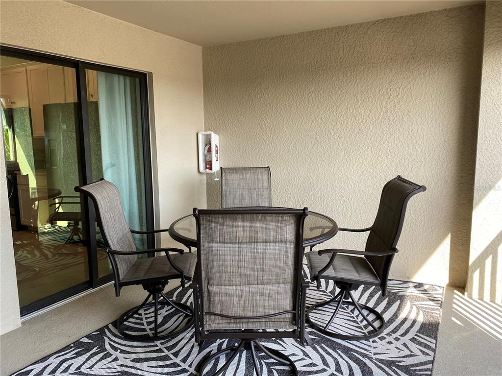 A covered patio features a glass-top dining table with four chairs on a patterned rug — 5664 PALMER CIRCLE UNIT 202, BRADENTON, FL