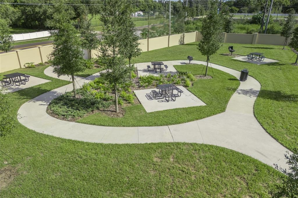 An outdoor park area features concrete walkways, picnic tables, grills, and young trees on grass — 2633 CAVANAUGH DRIVE, ORLANDO, FL