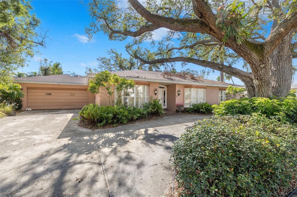 A single-story house with a tan exterior, a two-car garage, and a large oak tree — 215 SNELL ISLE BOULEVARD NE, ST PETERSBURG, FL
