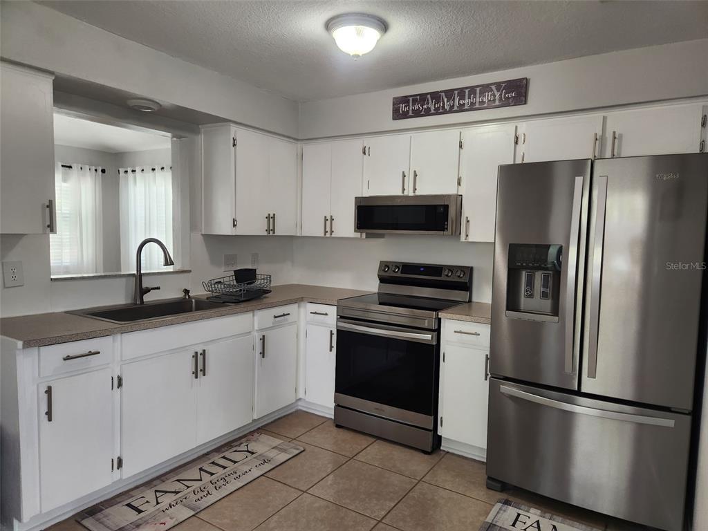 A kitchen features white cabinets, stainless steel appliances, and a sink with a window view — 865 7TH STREET S, SAFETY HARBOR, FL