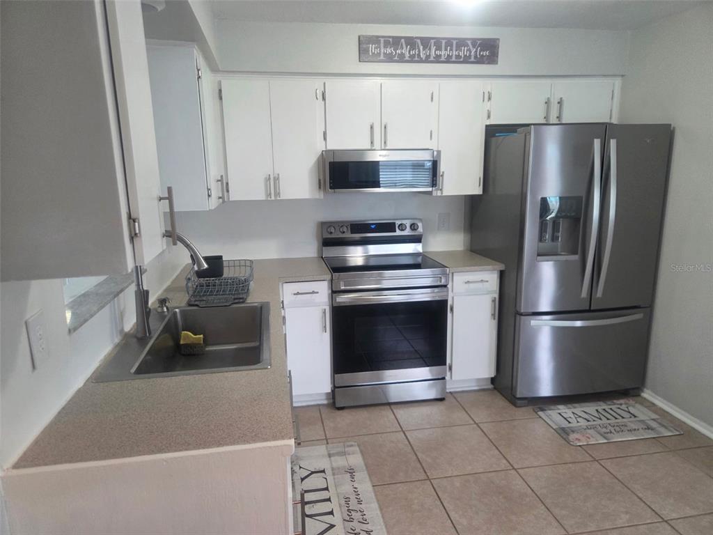 A kitchen features white cabinets, stainless steel appliances, a sink, and light-colored tile flooring — 865 7TH STREET S, SAFETY HARBOR, FL