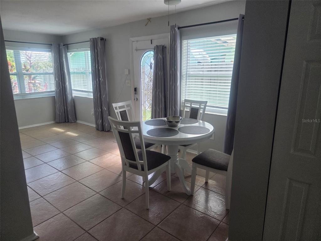 A dining area features a white table with four chairs, tiled flooring, and large windows — 865 7TH STREET S, SAFETY HARBOR, FL