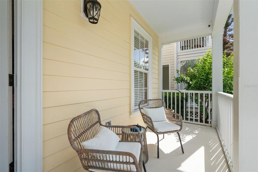 A covered balcony features light yellow siding, two wicker chairs, and a small side table — 206 NORFOLK PLACE, CELEBRATION, FL