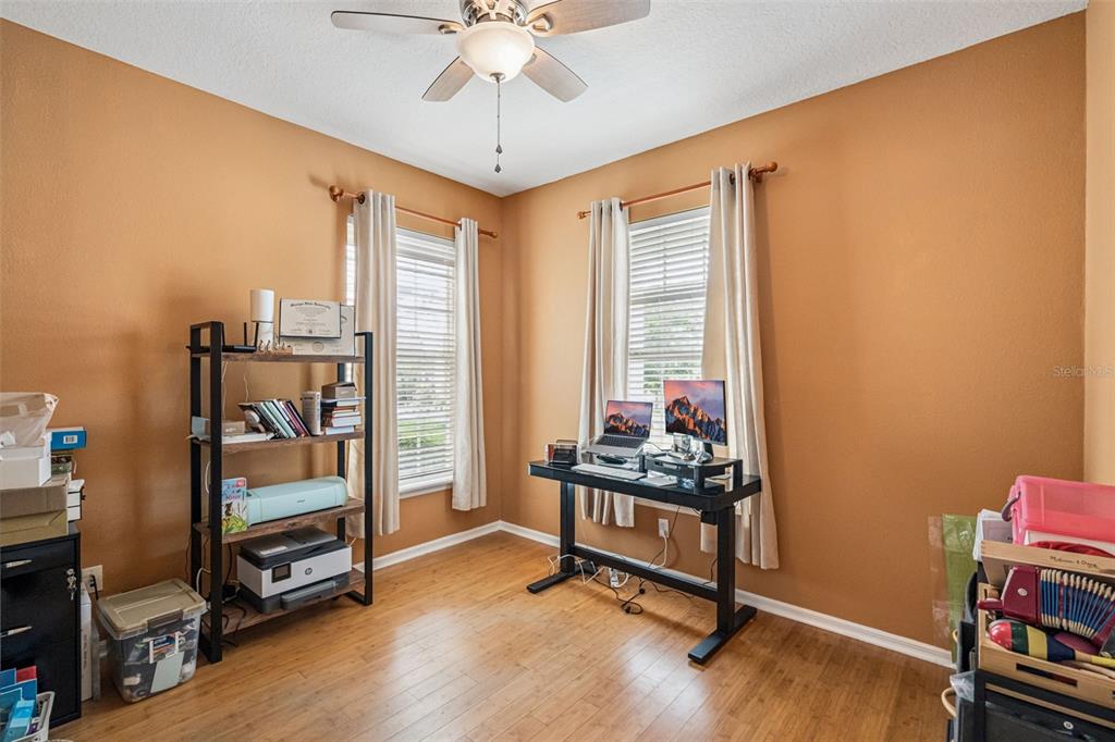 A home office features wood flooring, tan walls, a ceiling fan, and two windows with curtains — 206 NORFOLK PLACE, CELEBRATION, FL