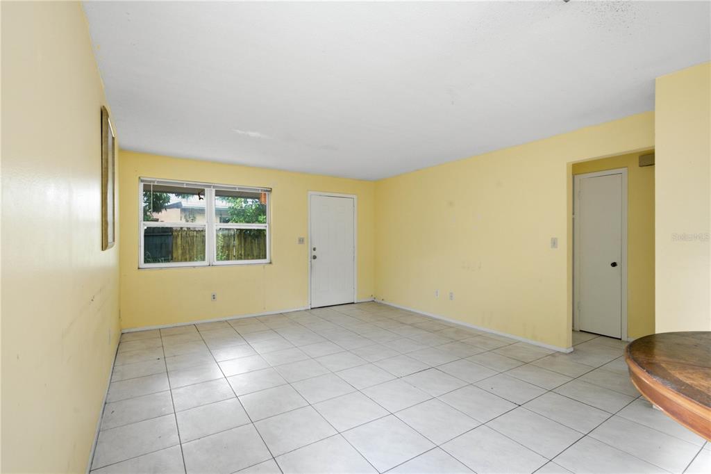 An empty room with yellow walls, white tile flooring, a window, and a white door — 1615 PALM WAY, LARGO, FL