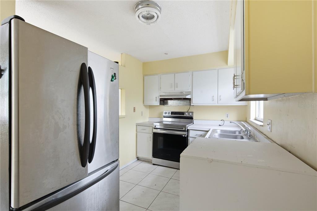 A kitchen features stainless steel appliances, white cabinets, yellow walls, and light-colored tile flooring — 1615 PALM WAY, LARGO, FL