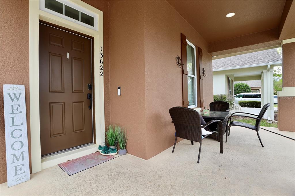 A covered front porch features a brown door, a welcome sign, and patio furniture — 13622 DARCHANCE ROAD, WINDERMERE, FL
