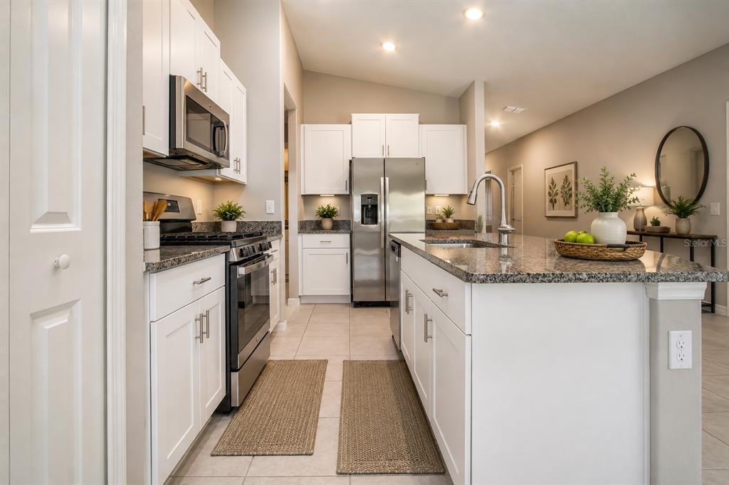 A kitchen with white cabinets, granite countertops, stainless steel appliances, and a central island — 9437 LEMON DROP LOOP, SUN CITY CENTER, FL