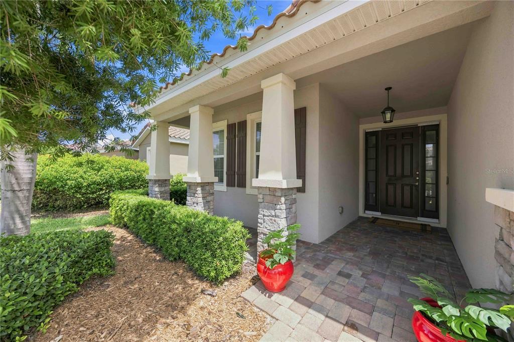 A covered front porch features stone-based columns, a paved floor, and a dark wood door — 5516 CARTAGENA DRIVE, SARASOTA, FL