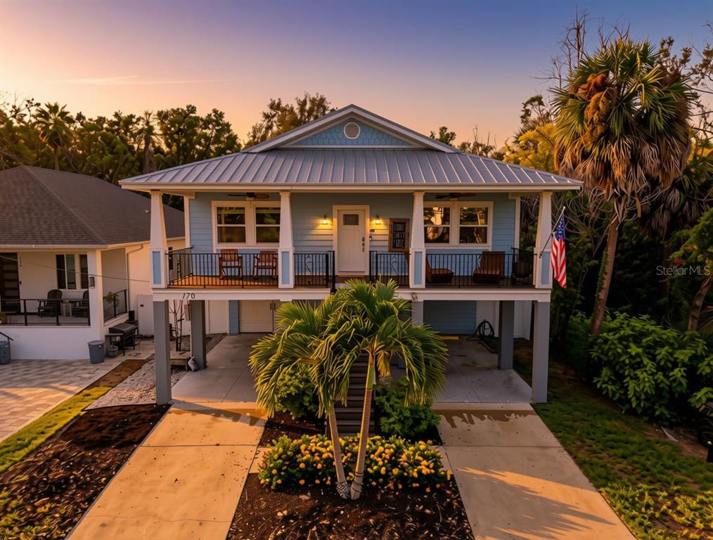 A light blue elevated house with a metal roof, front porch, and palm tree landscaping — 170 E SPRUCE STREET, TARPON SPRINGS, FL