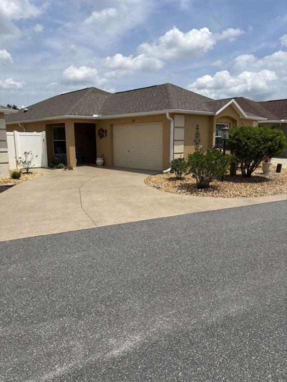 A tan single-story house with a two-car garage and a concrete driveway — 1067 CARVER COURT, THE VILLAGES, FL