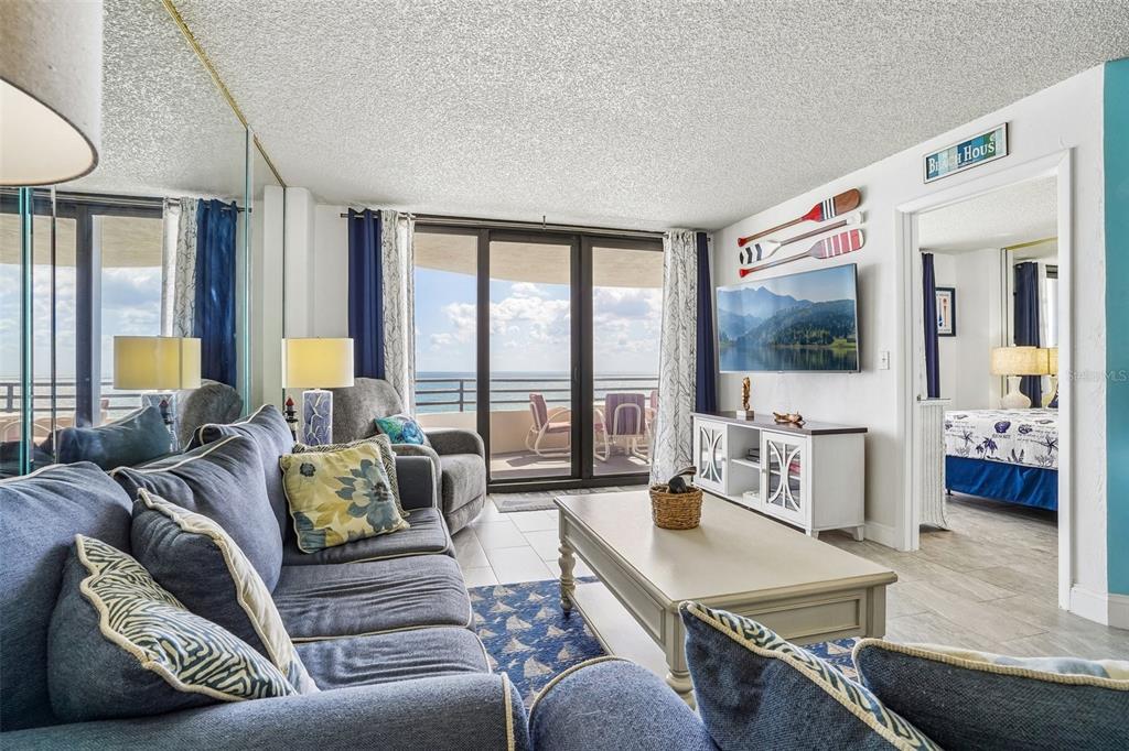 A living room features blue sofas, a coffee table, a patterned rug, and mirrored walls — 3115 S ATLANTIC AVENUE UNIT G030, DAYTONA BEACH, FL