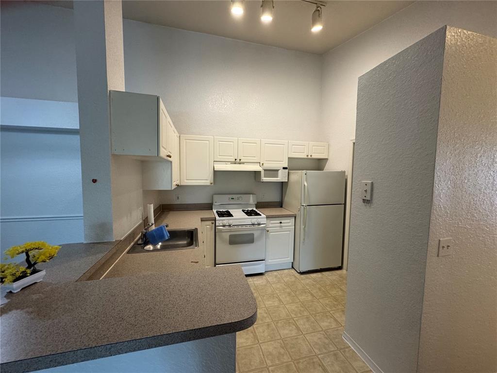 A kitchen features white cabinets, white appliances, a sink, and a gray countertop — 3325 S KIRKMAN ROAD UNIT 438, ORLANDO, FL