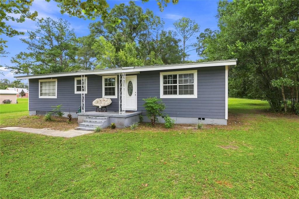 A single-story house with dark gray horizontal siding, a white front door, and a small porch — 16488 SW 139TH AVENUE, ARCHER, FL