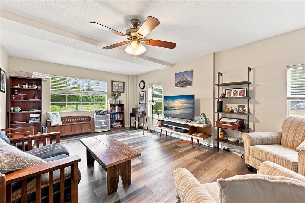 A living room features wood-look flooring, a ceiling fan, a television, and various bookshelves — 16488 SW 139TH AVENUE, ARCHER, FL